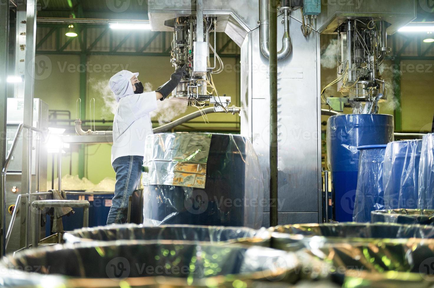 weiblich Arbeiter im ein Ketchup Fabrik kontrolliert automatisch aseptisch Füllung Maschine Füllung Ketchup in groß Bottiche beim ein industriell Einrichtung im Asien. Essen Industrie Agro-Industrie. foto