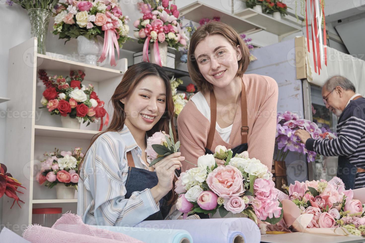 zwei junge schöne weibliche floristenpartner, die zusammen einen blumenstrauß arrangieren und dekorieren, lächeln mit glücklicher arbeit in einem farbenfrohen blumenladengeschäft mit frischen blüten, einem kleinen unternehmer. foto