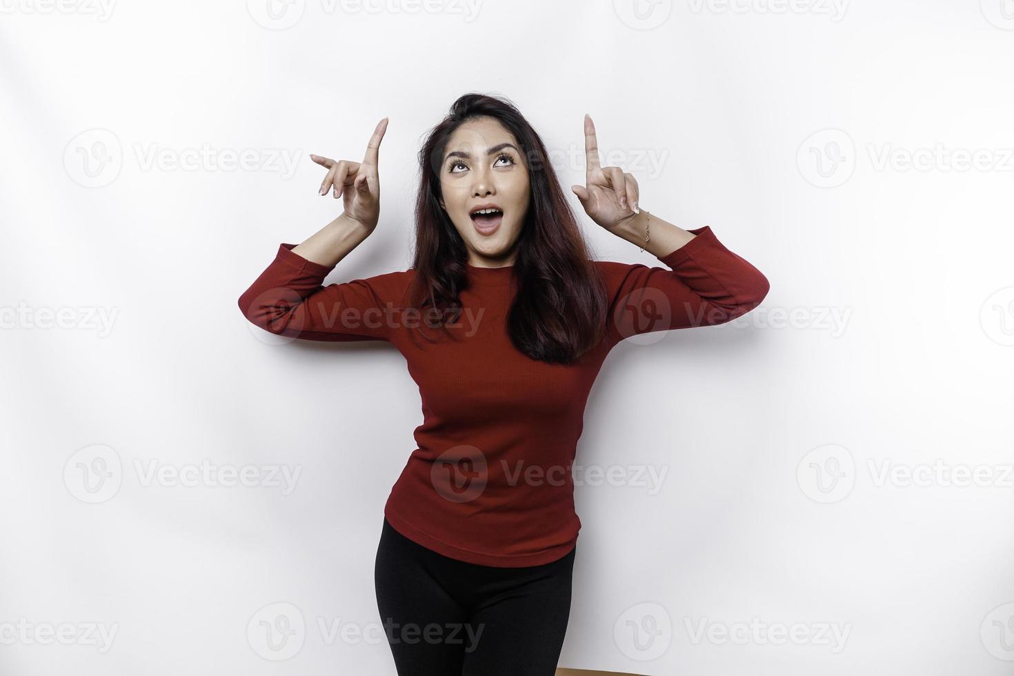 aufgeregt asiatisch Frau gekleidet im Rot, zeigen beim das Kopieren Raum auf oben von ihr, isoliert durch Weiß Hintergrund foto