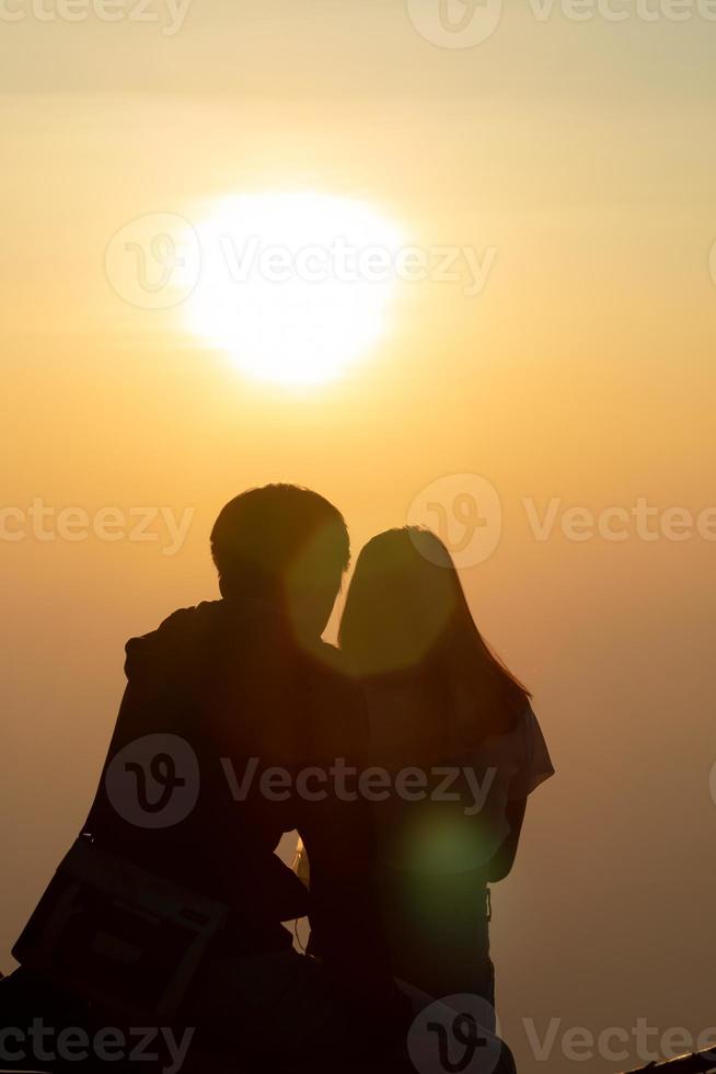 Silhouette von ein jung Paar Aufpassen das Sonnenuntergang während Dämmerung auf ein hoch Berg und Umarmen glücklich. glücklich Paar Umarmen jeder andere mit Liebe und Freundschaft und Freundlichkeit zum jeder andere. foto