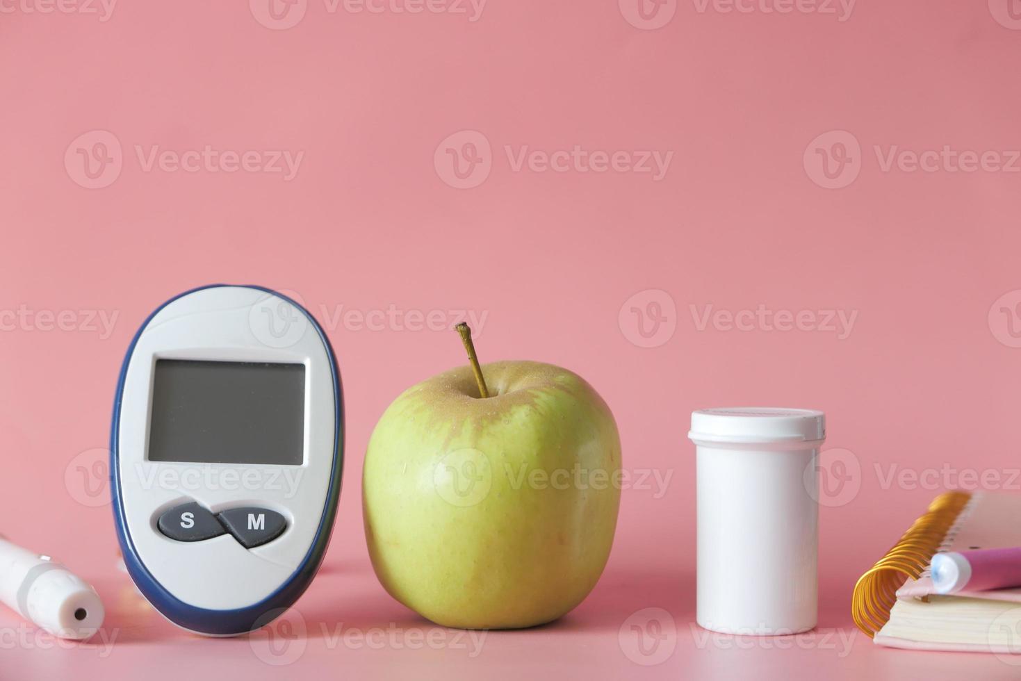 diabetische Messwerkzeuge und ein Apfel auf rosa Hintergrund foto