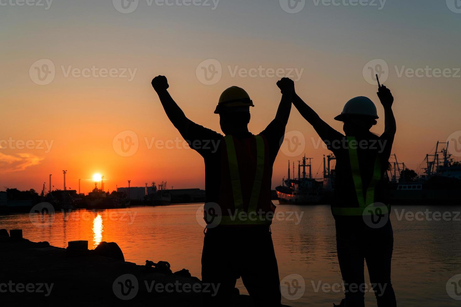 Silhouetten von Arbeiter und Ingenieur erziehen das Hand oben und Stehen auf das Werft. Hintergrund ist Öl Lager Silo. Zusammenarbeit Zusammenarbeit und Erfolg im Arbeiten zusammen Konzept. foto
