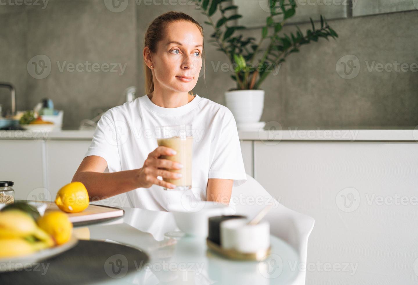 jung schlank Frau im Weiß T-Shirt und Blau Jeans Trinken Obst Smoothie gesund Essen im Küche beim Zuhause foto