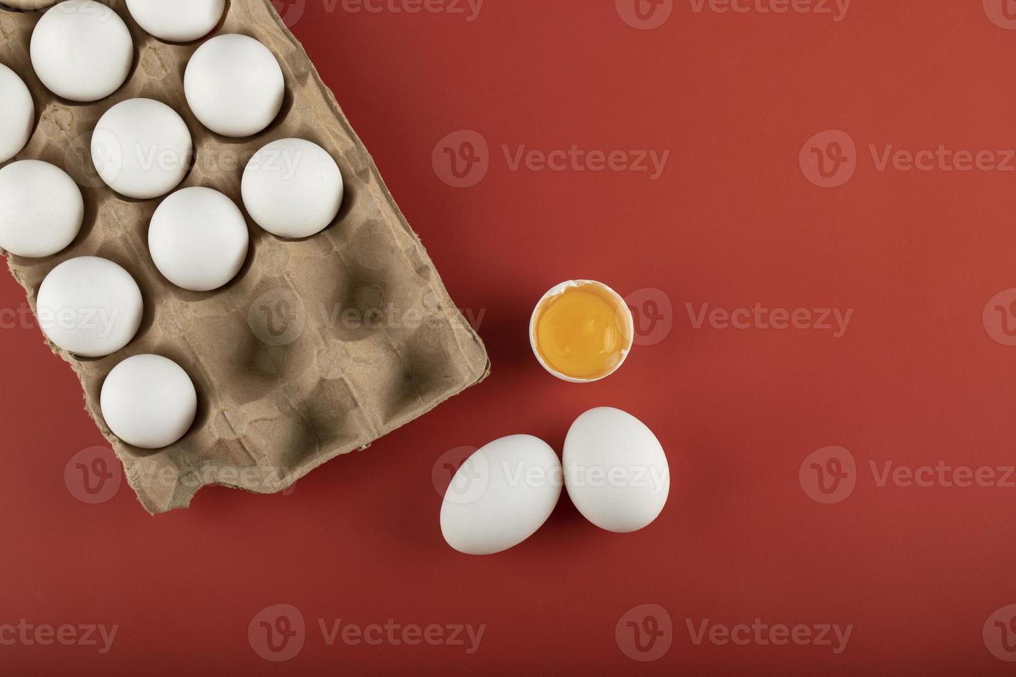 Karton der weißen Eier mit einem Eigelb auf einem roten Hintergrund foto