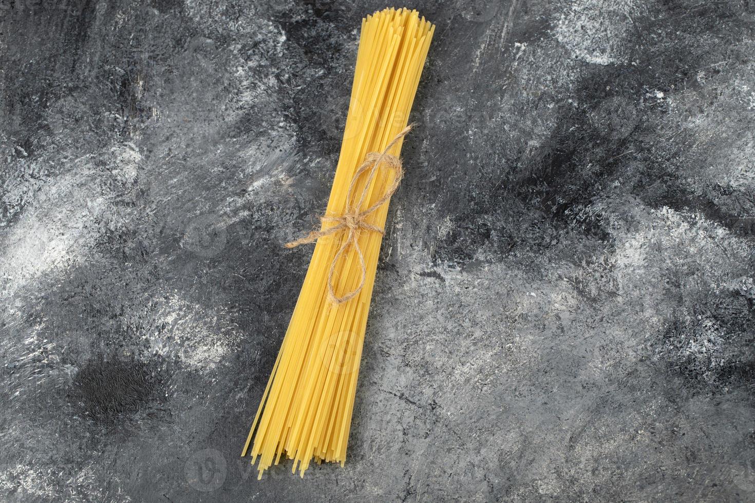 trockene Spaghetti mit einem Seil auf einem Marmorhintergrund gebunden foto