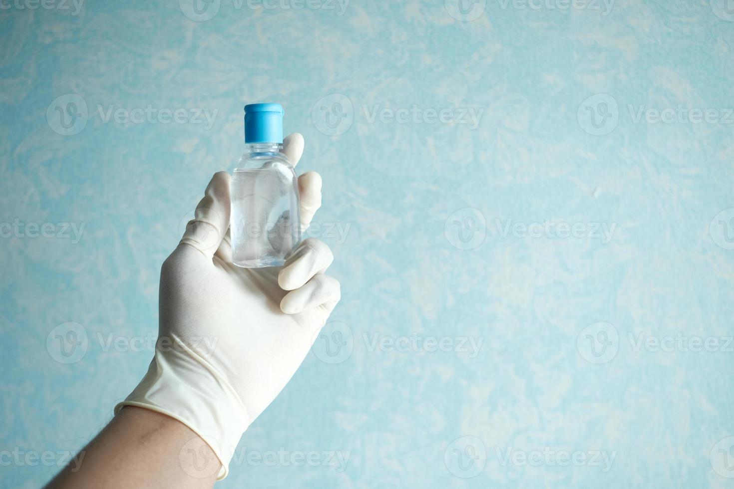 Hand in Latexhandschuh halten Händedesinfektionsmittel mit Kopierraum foto