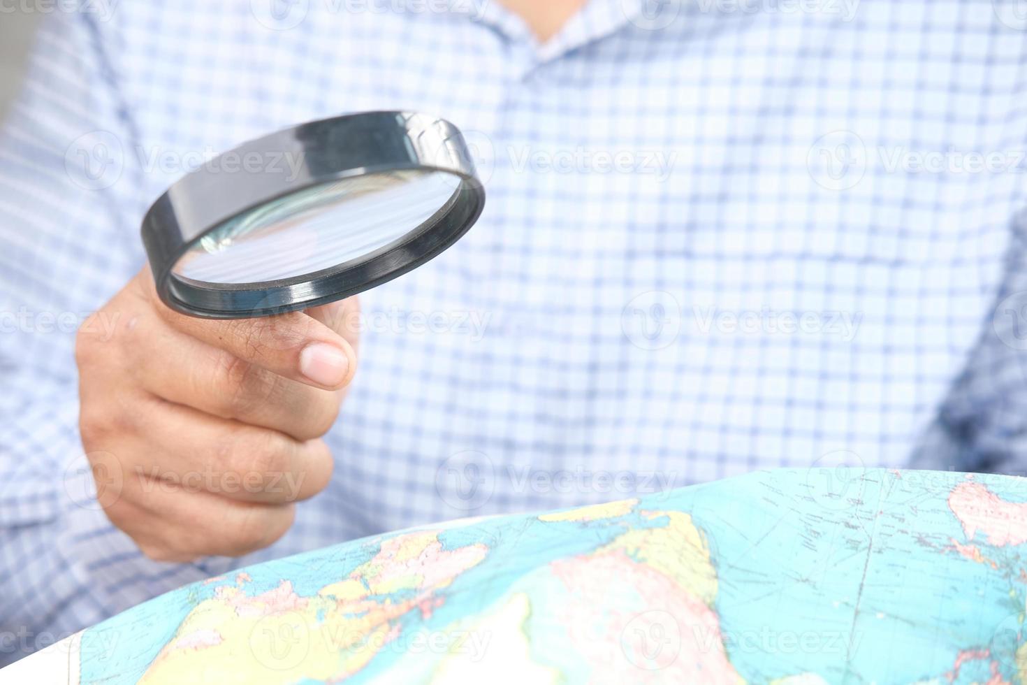 Person, die eine Lupe benutzt, um eine Weltkarte zu betrachten foto