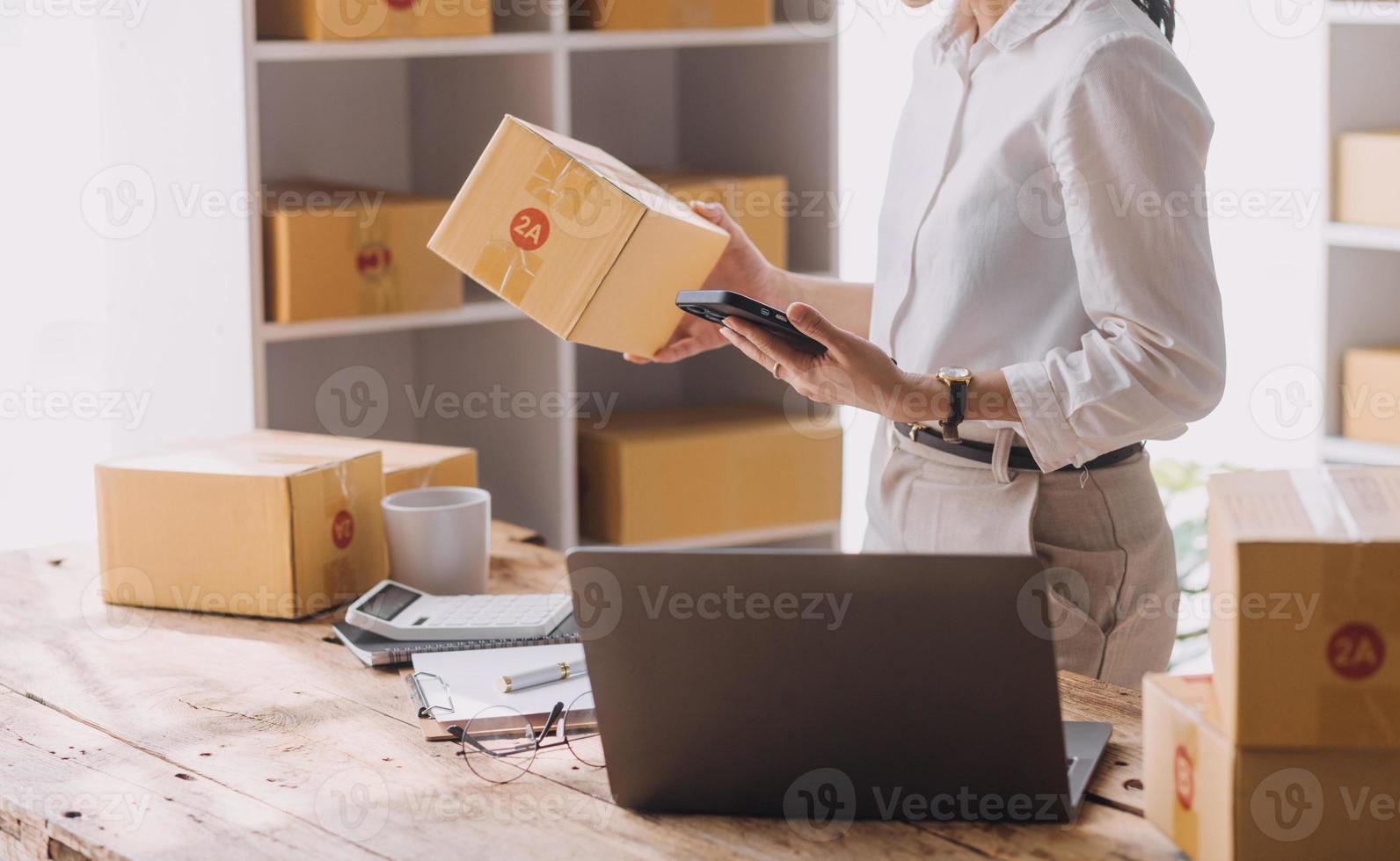 Start-up-KMU-Kleinunternehmer einer freiberuflich tätigen Asiatin, die einen Laptop mit Box verwendet fröhlicher Erfolg Asiatin ihre Hand hebt die Online-Marketing-Verpackungsbox und das Konzept der KMU-Ideenlieferung an foto