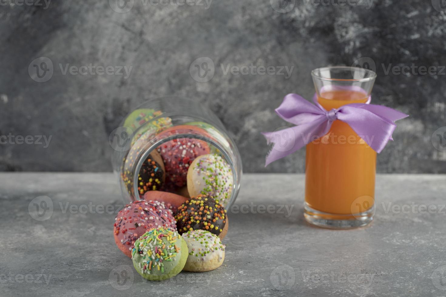 ein Glas voller kleiner bunter Donuts mit einer Glasflasche Orangensaft foto