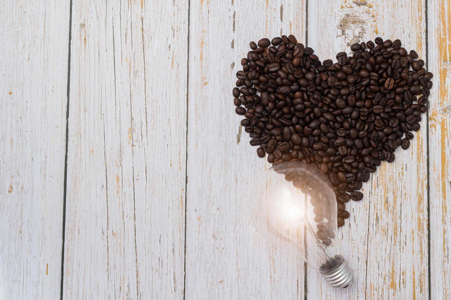 Kaffeebohnen in Herzform und eine Glühbirne auf einem Holztisch foto