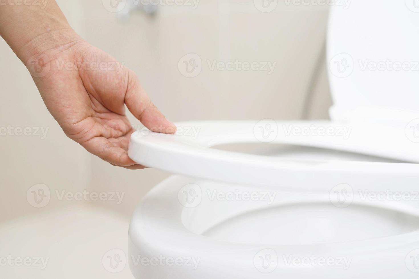 schließen oben Hand von ein Frau Schließen das Deckel von ein Toilette Sitz. Hygiene und Gesundheit Pflege Konzept. foto