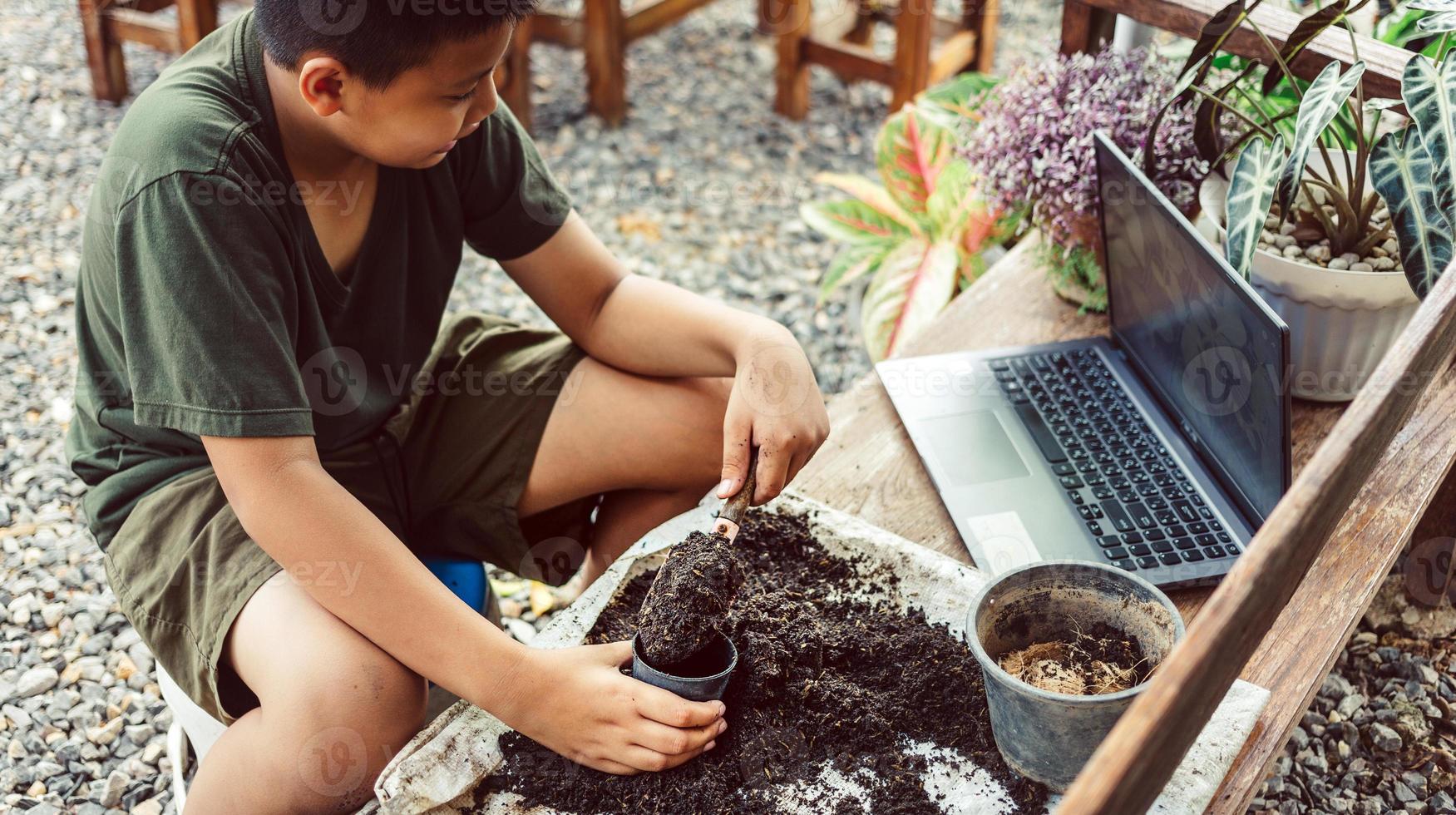 Junge lernt durch Online-Unterricht, Blumen in Töpfen anzubauen. Erde in Töpfe schaufeln, um Pflanzen für das Pflanzen von Freizeitaktivitäten vorzubereiten foto