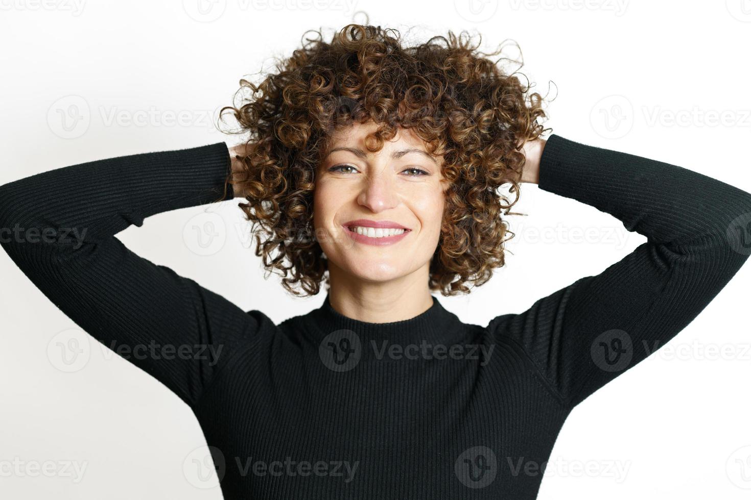 glücklich Frau mit lockig Haar lächelnd mit Hände hinter foto