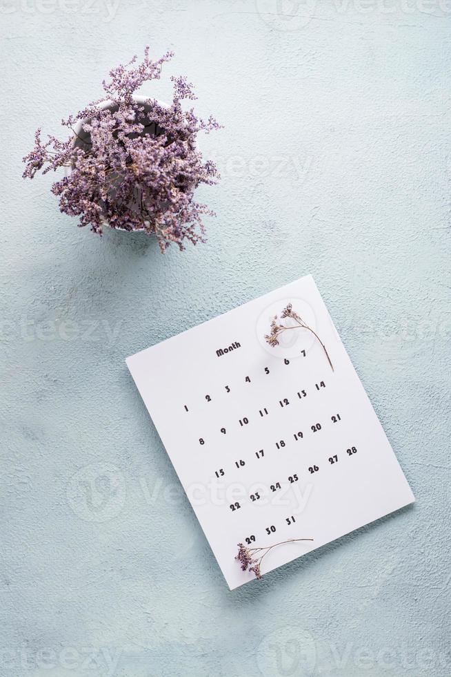 leer Blatt von das monatlich Kalender und ein Strauß von getrocknet Blumen auf das Tisch. Zeit Planung und Organisation. Vertikale Aussicht foto