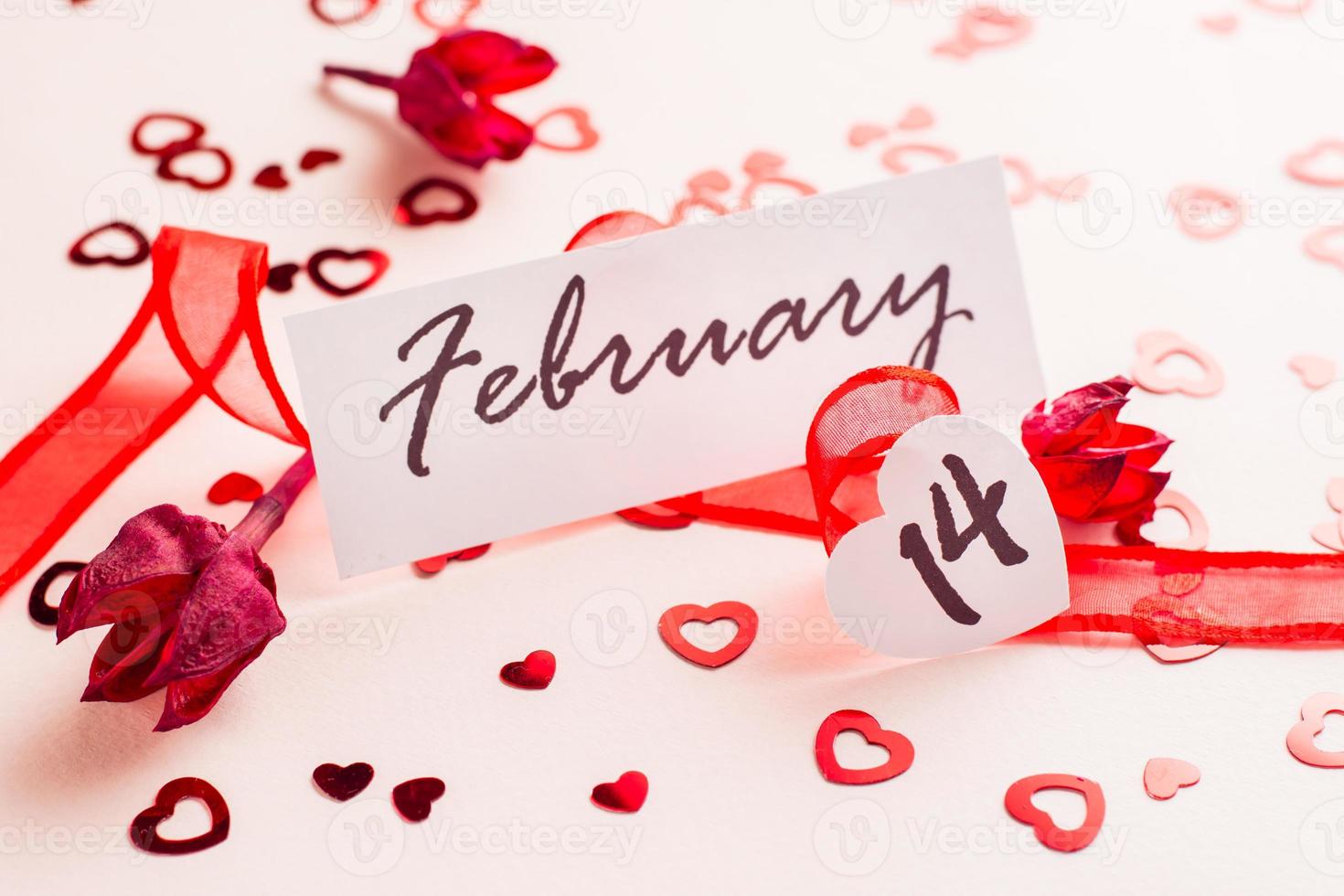 Valentinstag Tag. das Datum von Februar 14 steht im ein rot Band und ein trocken Blume auf ein Rosa Hintergrund übersät mit Herzen foto