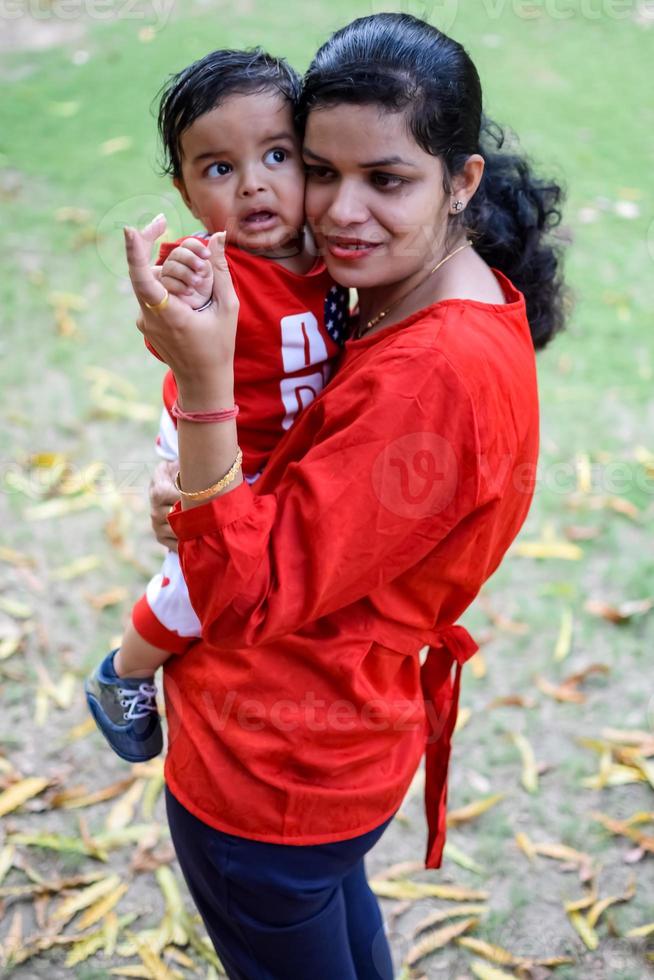 liebend Mama Tragen von ihr Baby beim Gesellschaft Park. hell Porträt von glücklich Mama halten Kind im ihr Hände. Mutter umarmen ihr wenig 9 Monate alt Sohn. foto