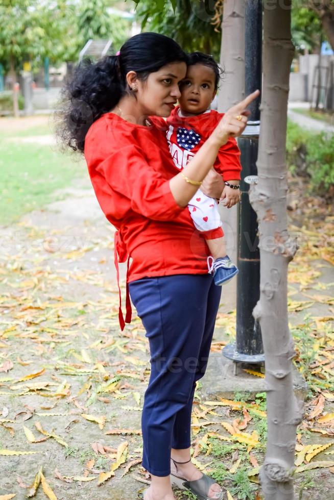liebend Mama Tragen von ihr Baby beim Gesellschaft Park. hell Porträt von glücklich Mama halten Kind im ihr Hände. Mutter umarmen ihr wenig 9 Monate alt Sohn. foto