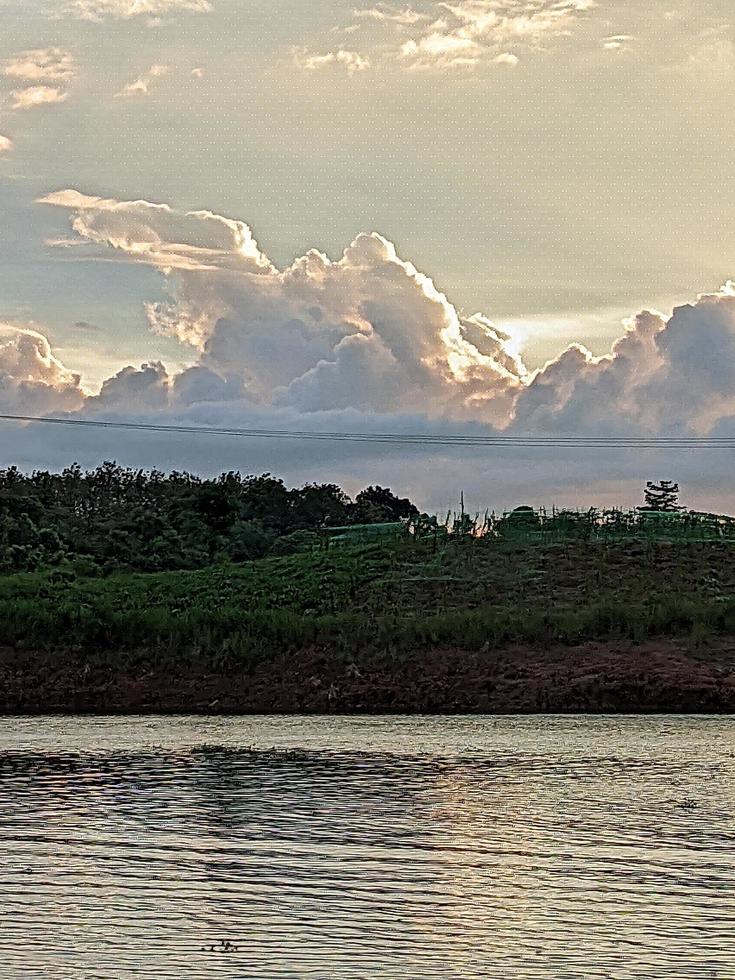 ein Boot ist im das Wasser und das Himmel ist Blau und das Wasser ist Ruhe. ein Baum im das Vordergrund mit das Sonne leuchtenden durch das Wolken. das Wasser ist Ruhe. foto