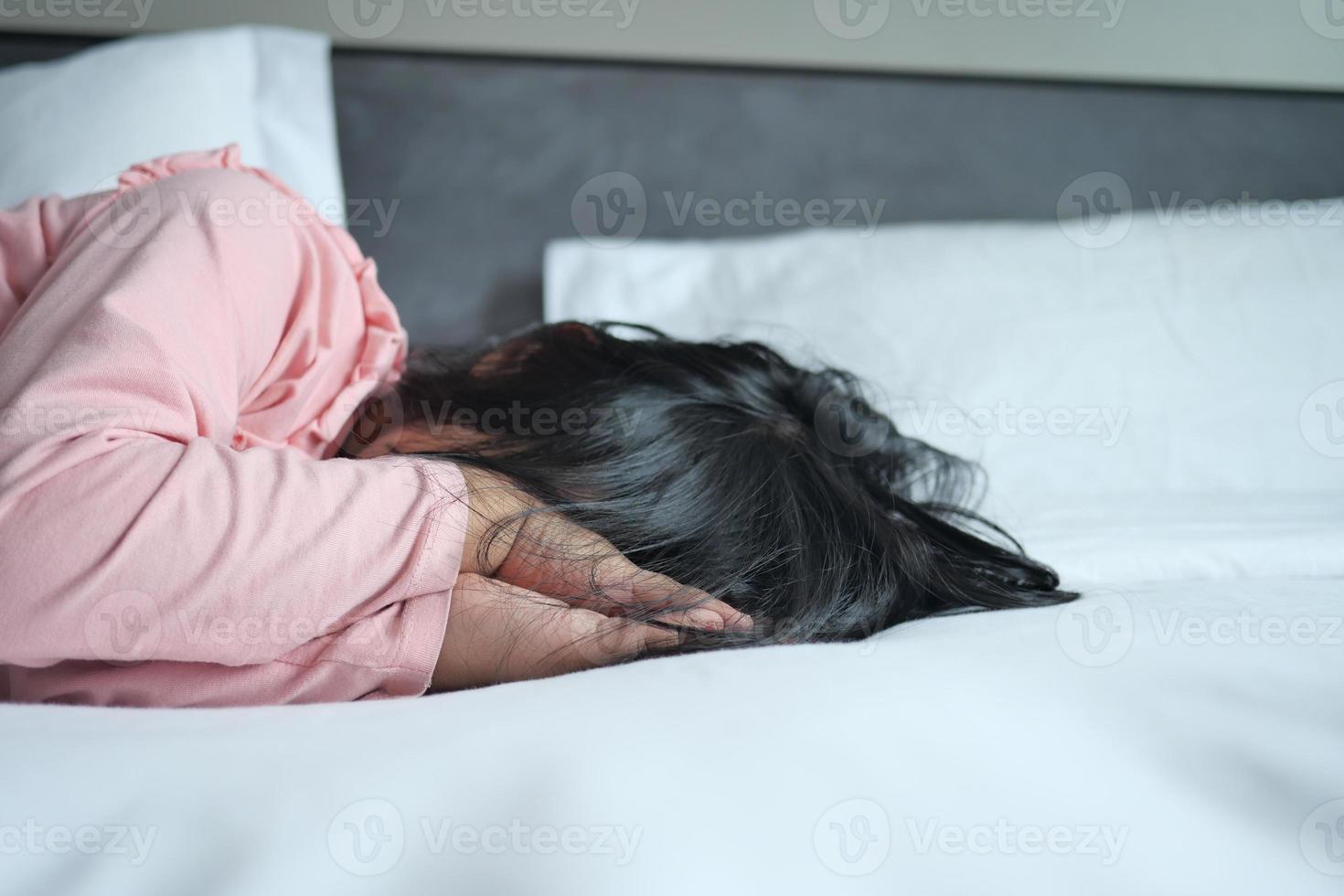ein verärgert Kind Mädchen Startseite ihr Gesicht mit Hand auf Bett foto