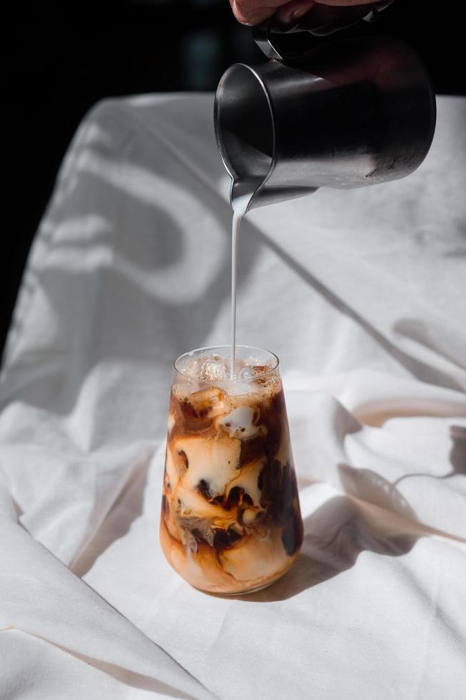 Barista gießt Milch in ein Glas Eiskaffee foto