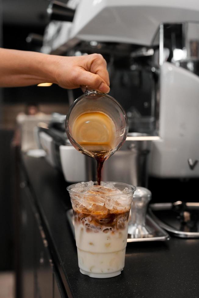 Barista gießt Milch in ein Glas Eiskaffee foto