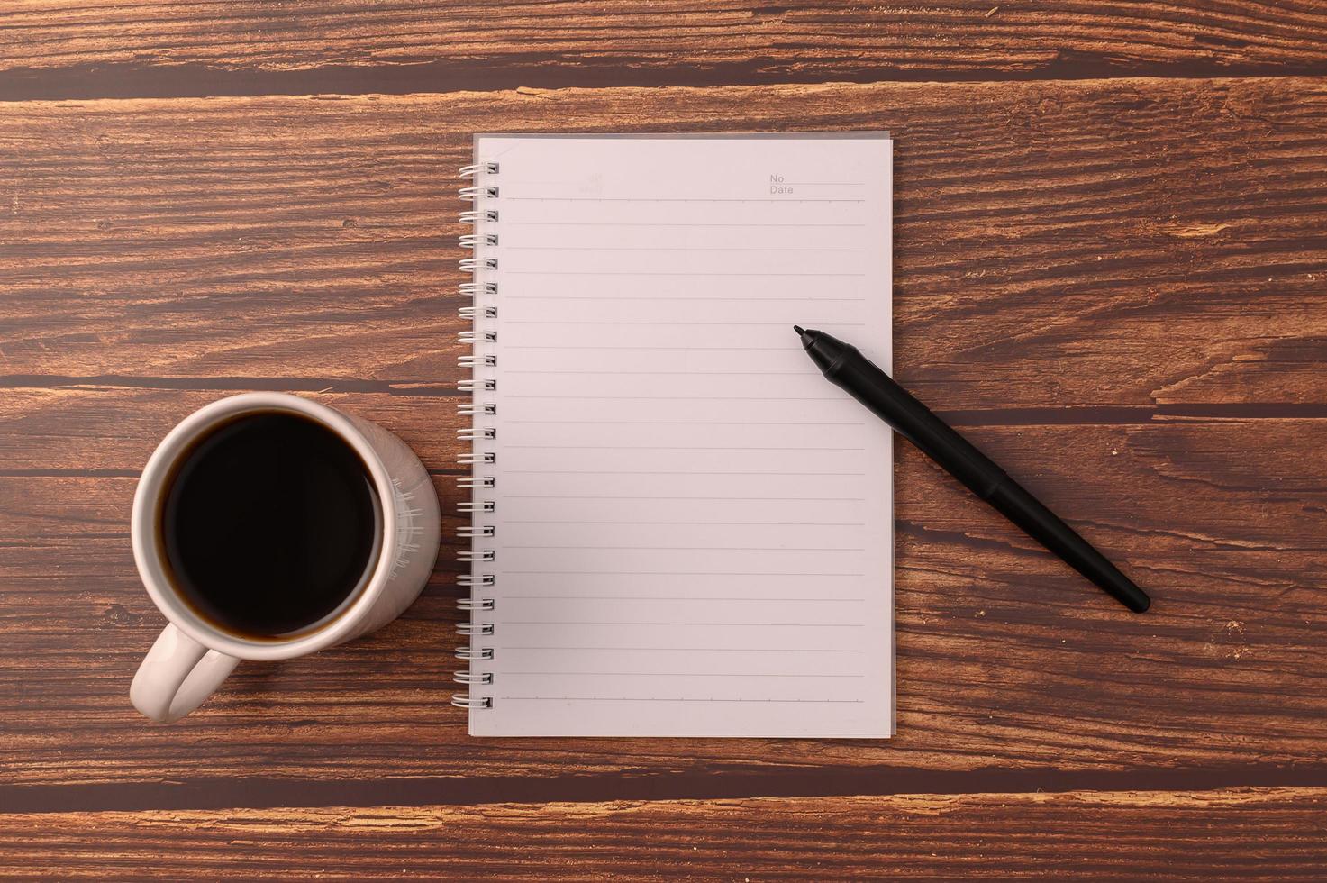 Kaffee und ein Notizbuch mit einem Stift auf einem Holzschreibtisch foto