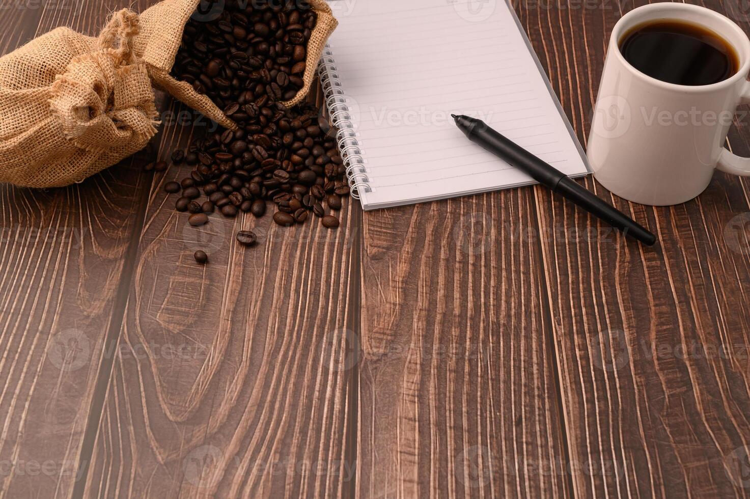 Kaffee, Kaffeebohnen und ein Notizbuch mit einem Stift auf einem Holzschreibtisch foto