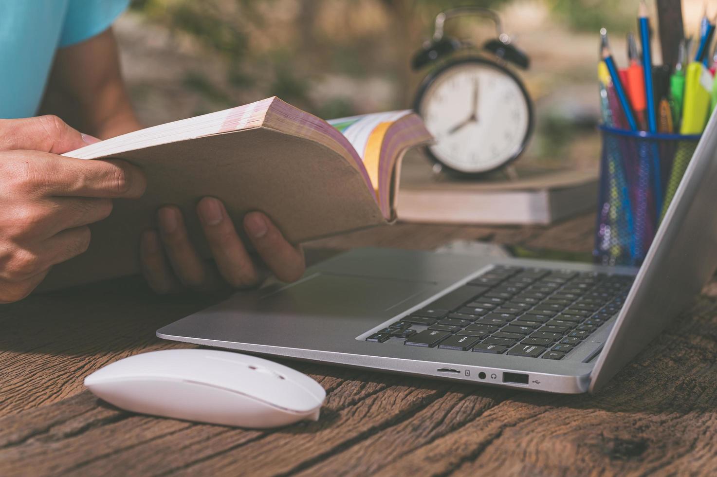 eine Person, die ein Buch vor einem Computer liest foto