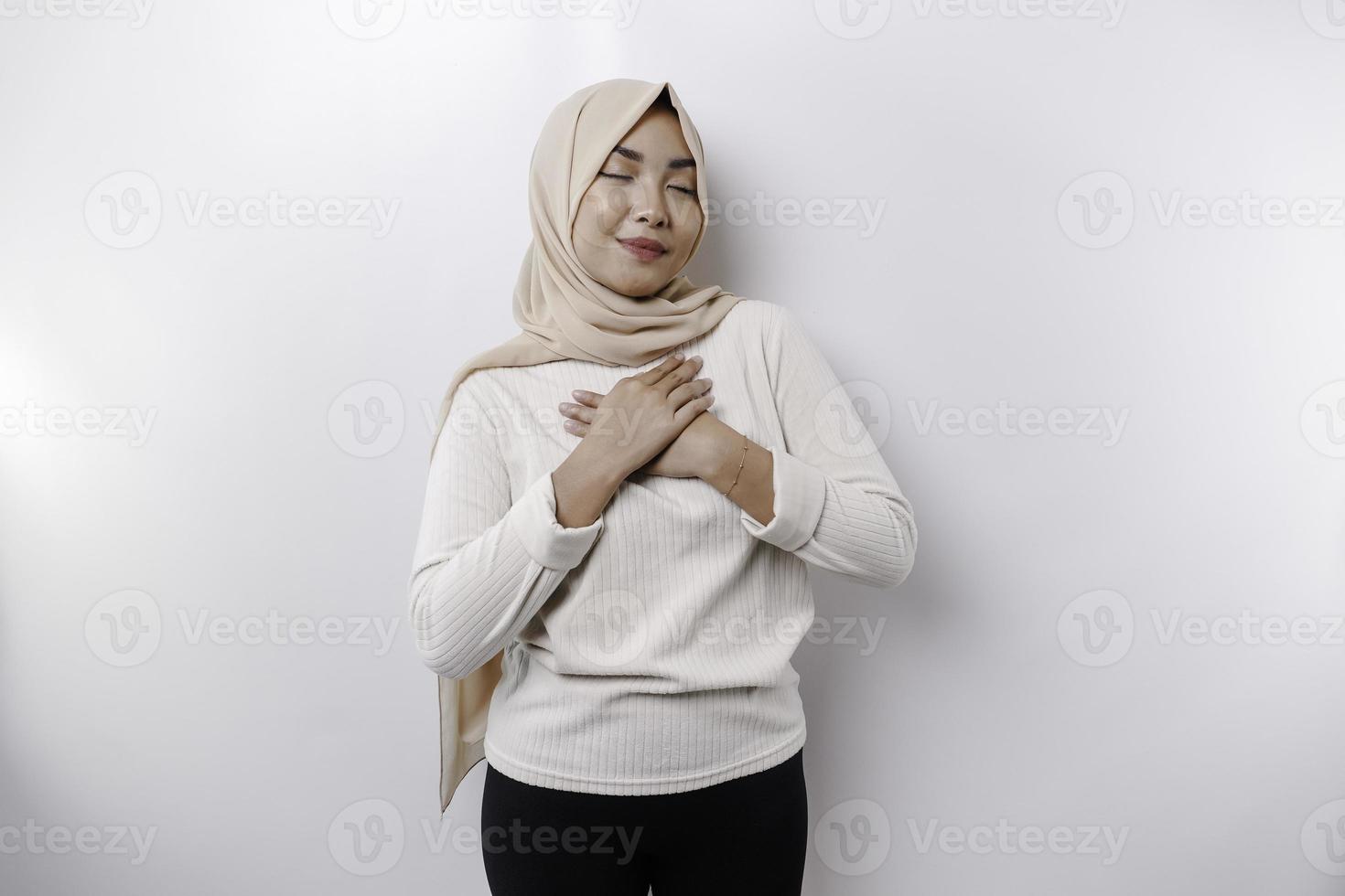 glücklich achtsam dankbar jung asiatisch Muslim Frau mit ihr Hand auf ihr Truhe lächelnd isoliert auf Weiß Hintergrund foto