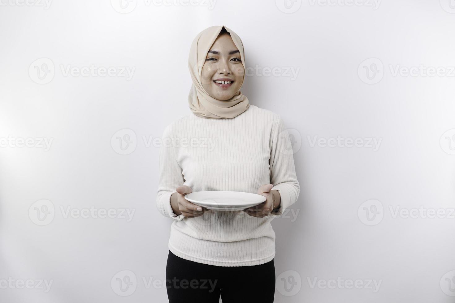 ein asiatisch Muslim Frau ist Fasten und hungrig und halten ein Teller während suchen beiseite Denken Über Was zu Essen foto