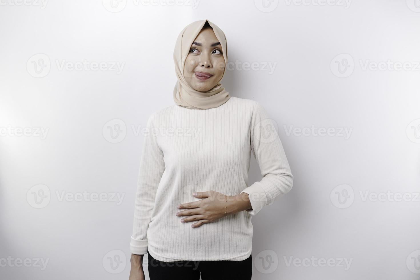 ein asiatisch Muslim Frau ist Fasten und hungrig und berühren ihr Bauch während suchen beiseite Denken Über Was zu Essen foto