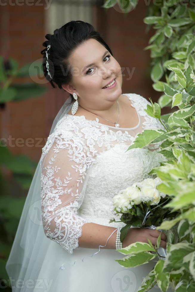 Vertikale Porträt von ein dunkelhaarig Fett Braut mit ein Hochzeit Strauß. foto