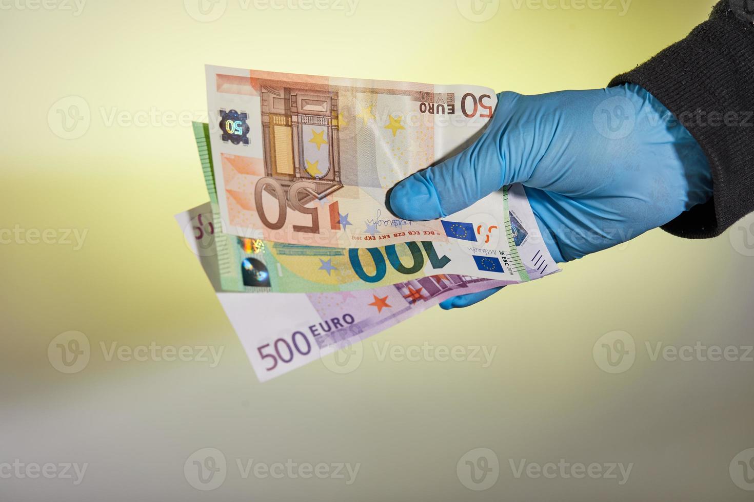 Die Hand eines Mannes in einem blauen medizinischen Handschuh hält Geld in Form von Euro-Scheinen foto