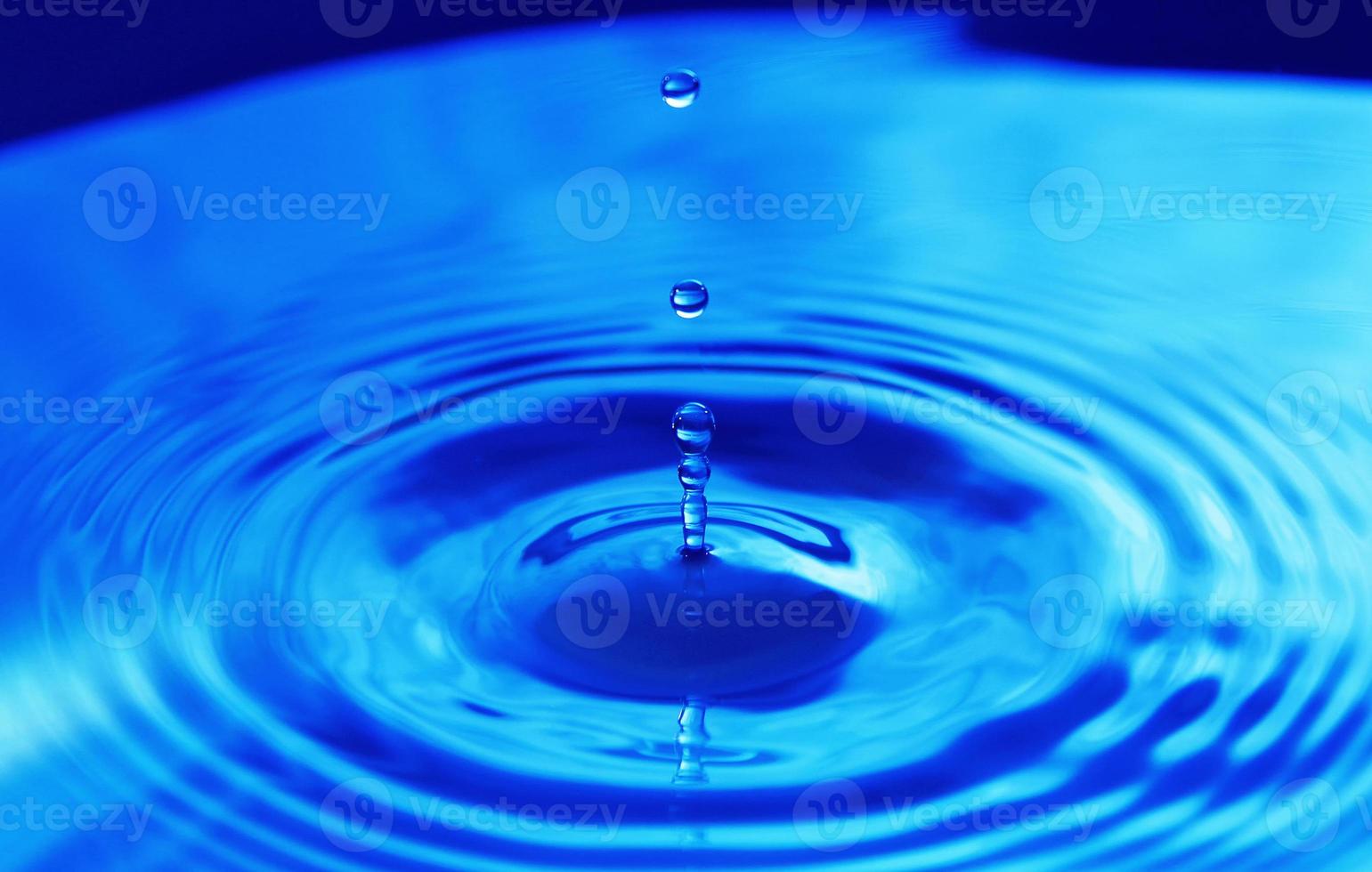 Tropfen, die im Wasser auf blauem Hintergrund fallen foto