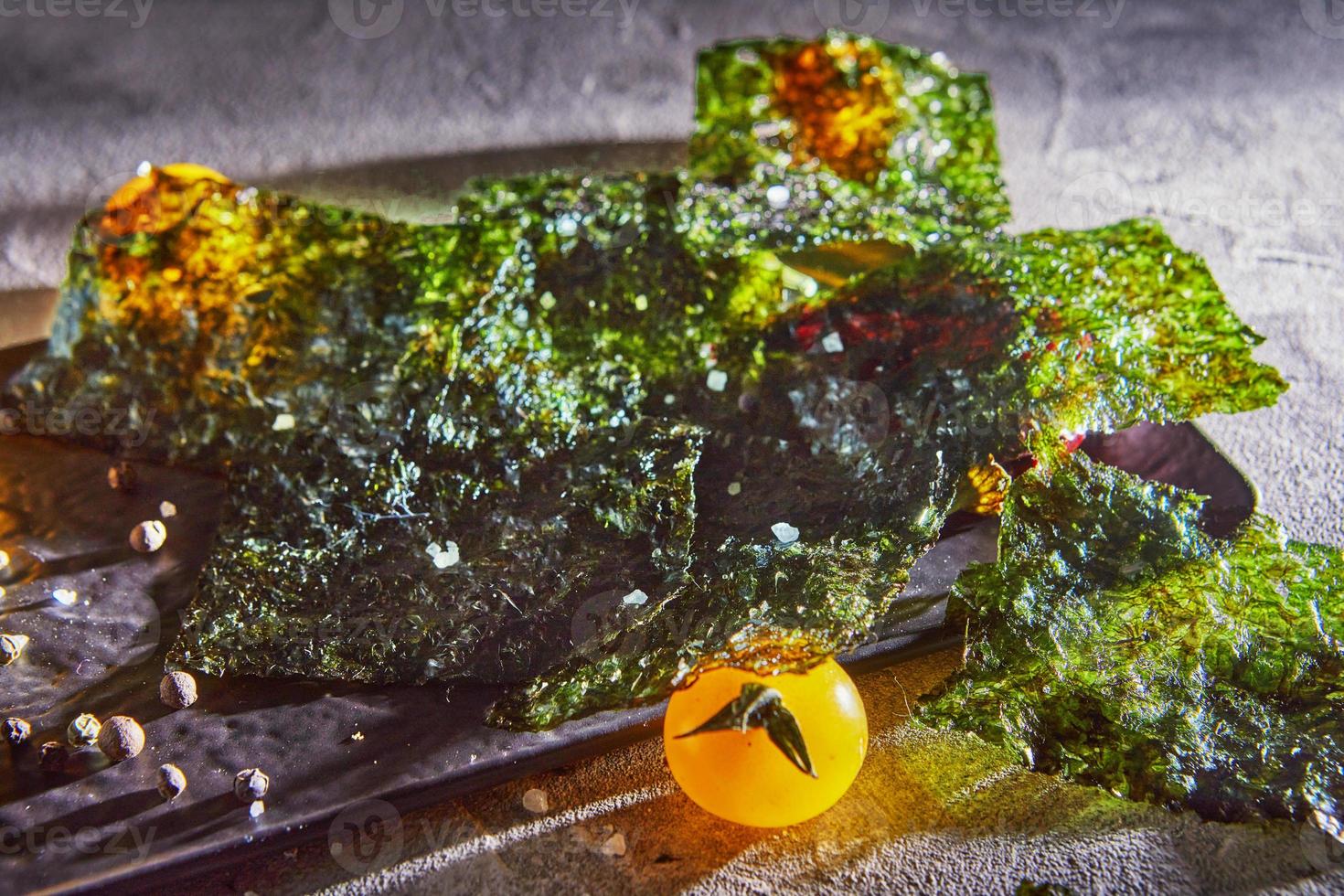 knuspriger Nori-Seetang mit Kirschtomaten und dunklen Gewürzen auf grauem Beton foto