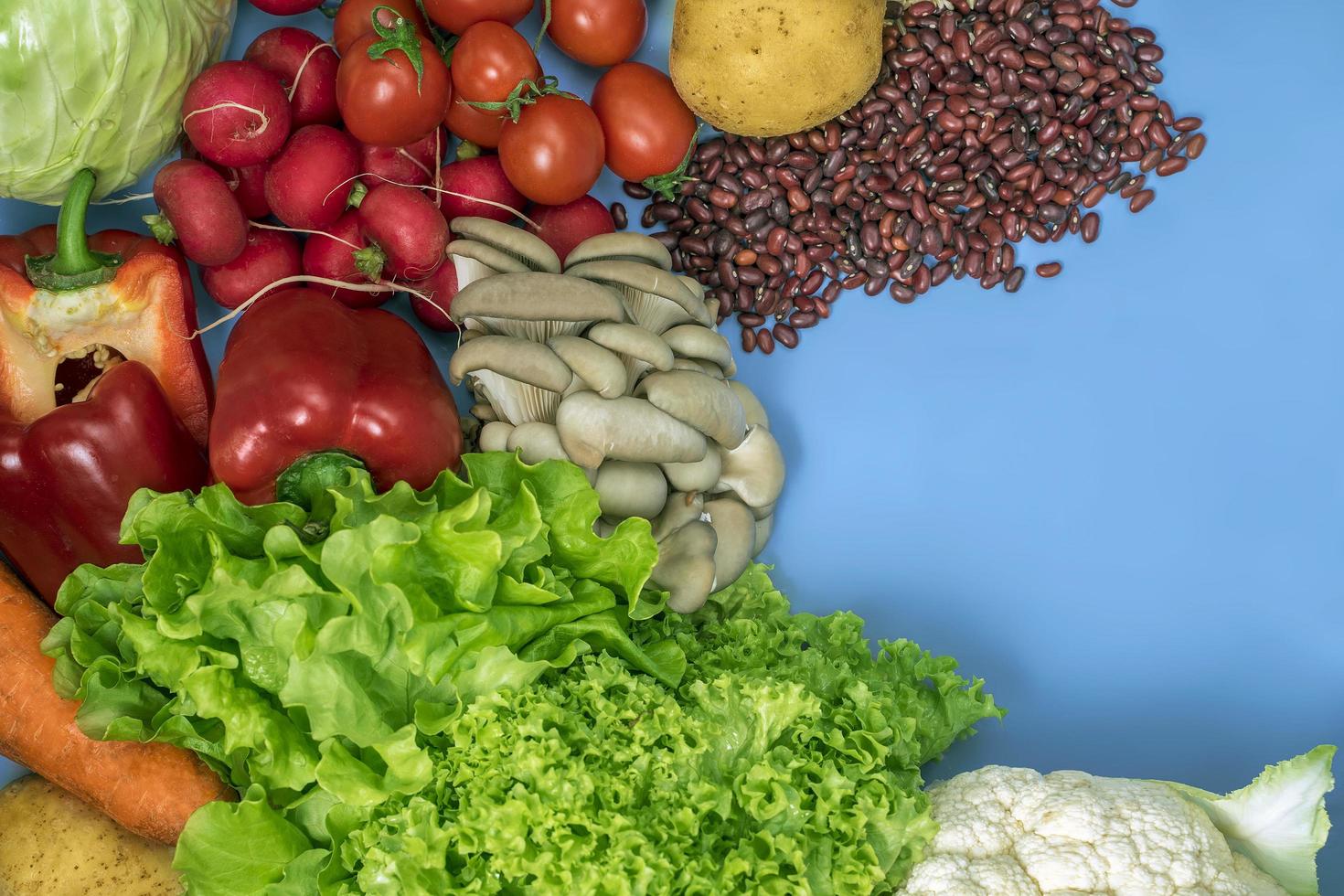 Produkte für eine vegetarische Entgiftungsdiät von Blumenkohl, Salat, Radieschen, Tomaten, Pilzen, Bohnen und rotem Paprika auf blauem Grund foto