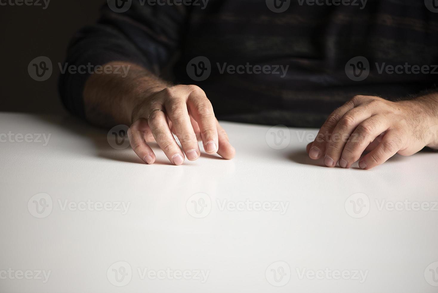 unerkennbarer Mann in einer vertrauten Position, der an einem weißen leeren Tisch sitzt foto