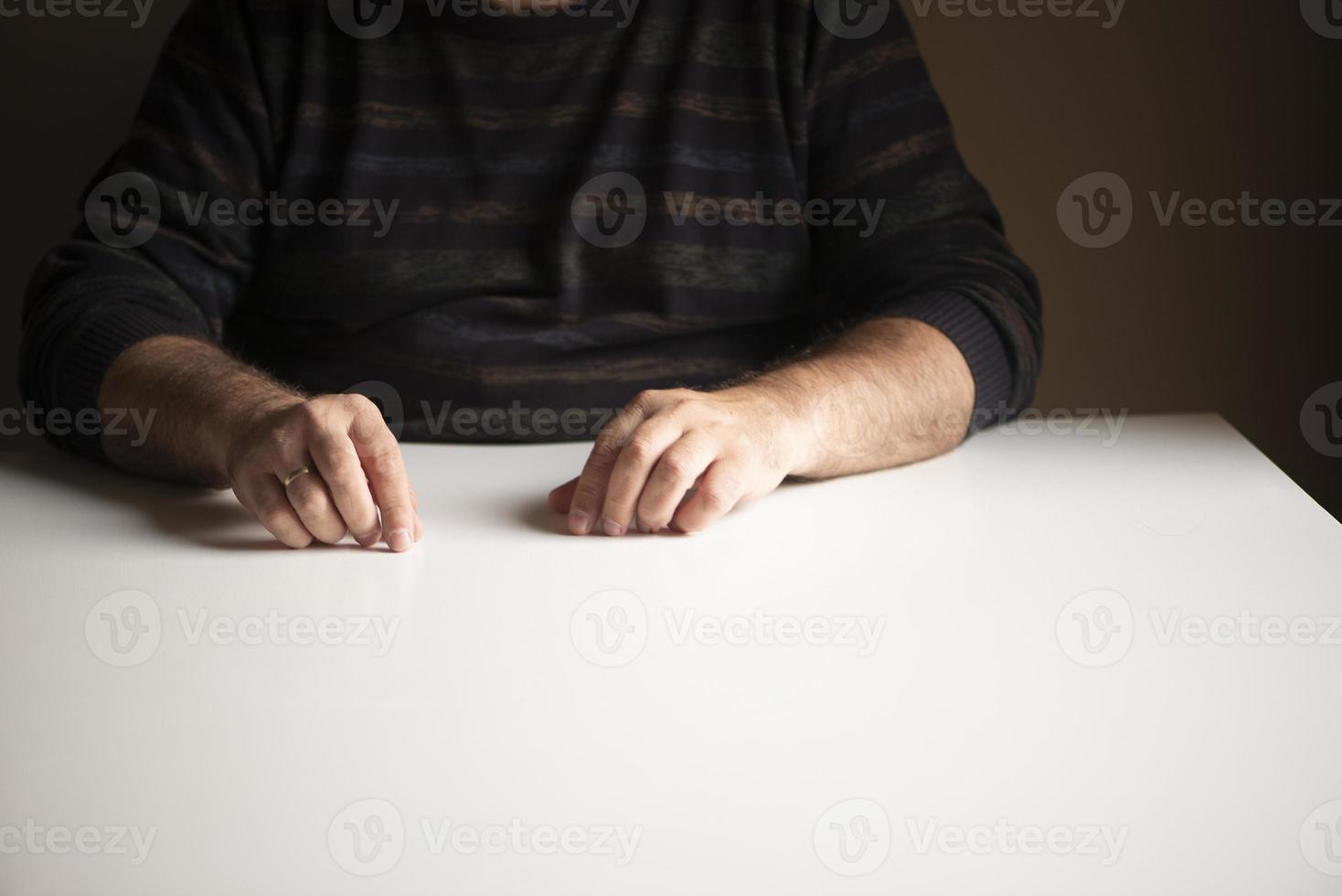 unerkennbarer Mann in einer vertrauten Position, der an einem weißen leeren Tisch sitzt foto