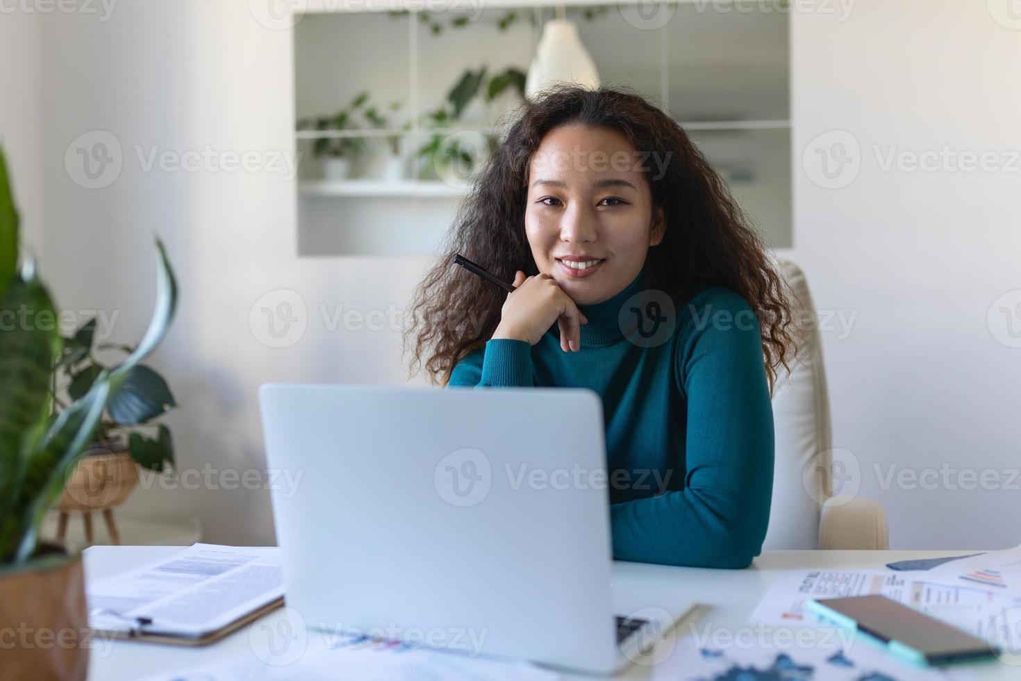 Schuss von asiatisch lächelnd Geschäft Frau Arbeiten mit Laptop während suchen beim Kamera im modern Anfang Büro. foto