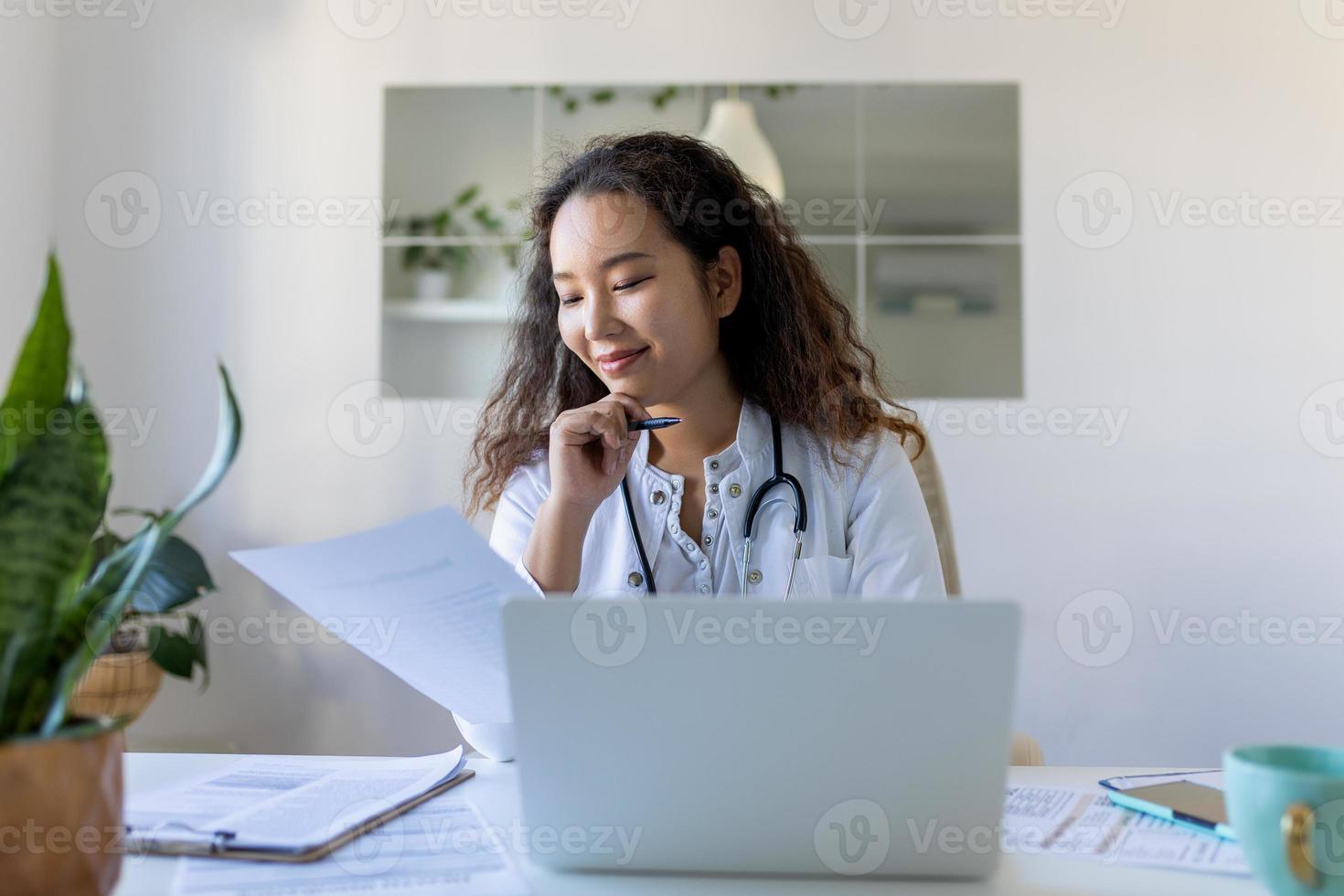 Arzt Fachmann weiblich asiatisch Arzt tragen Uniform nehmen Anmerkungen im medizinisch Tagebuch, Füllung Unterlagen, geduldig Krankheit Geschichte, suchen beim Laptop Bildschirm, Schüler Aufpassen Webinar foto