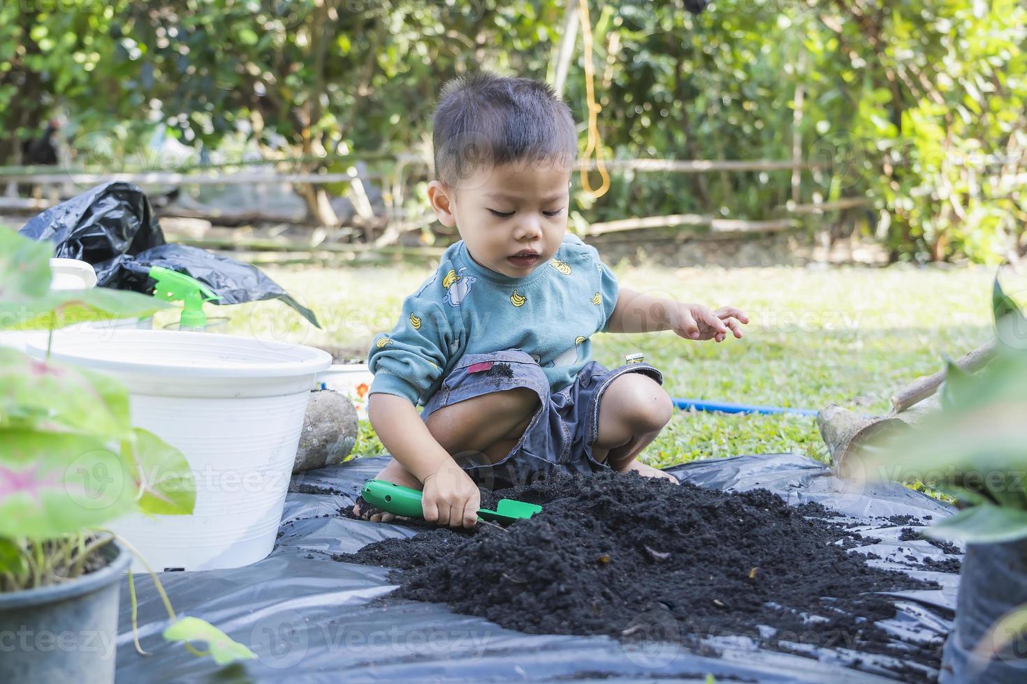 kleines kind schaufelt erde in töpfe, um pflanzen zum pflanzen vorzubereiten. kleinkindjunge, der erde zum pflanzen für den kleinen helfer der mutter gräbt. Gartenarbeit. hobbys zu hause gartenbau. freizeitkonzept foto