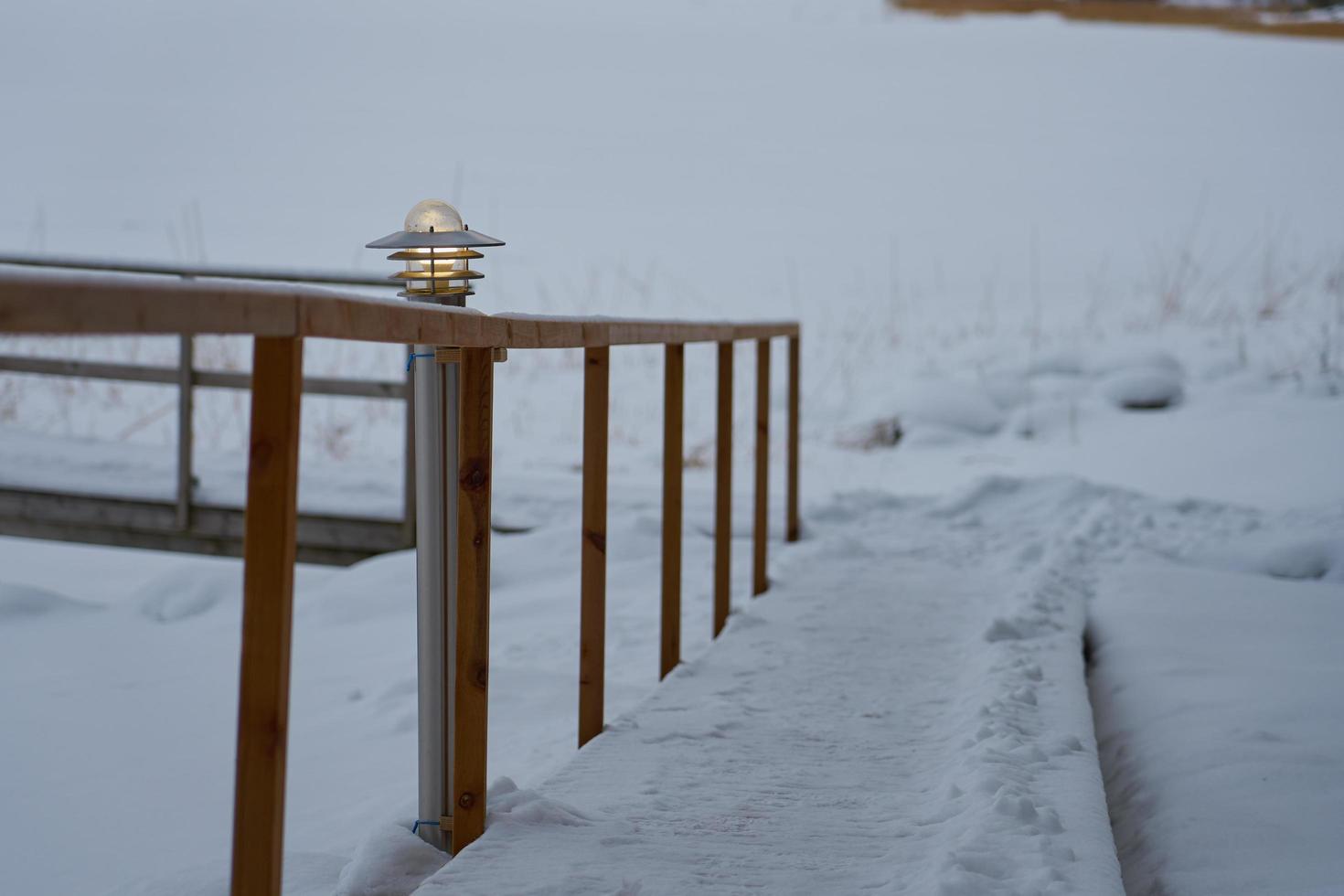 Laterne auf einem schneebedeckten Weg mit Holzgeländern im Winter foto