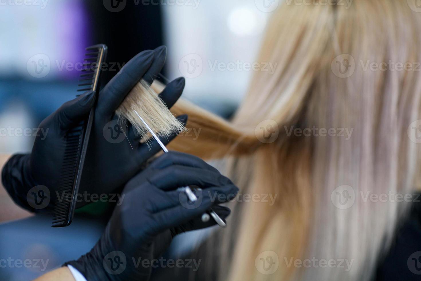 ein Friseur im Gummi Handschuhe hält ein Paar von Schere und ein Kamm. Frau bekommen ein Neu Haarschnitt. foto