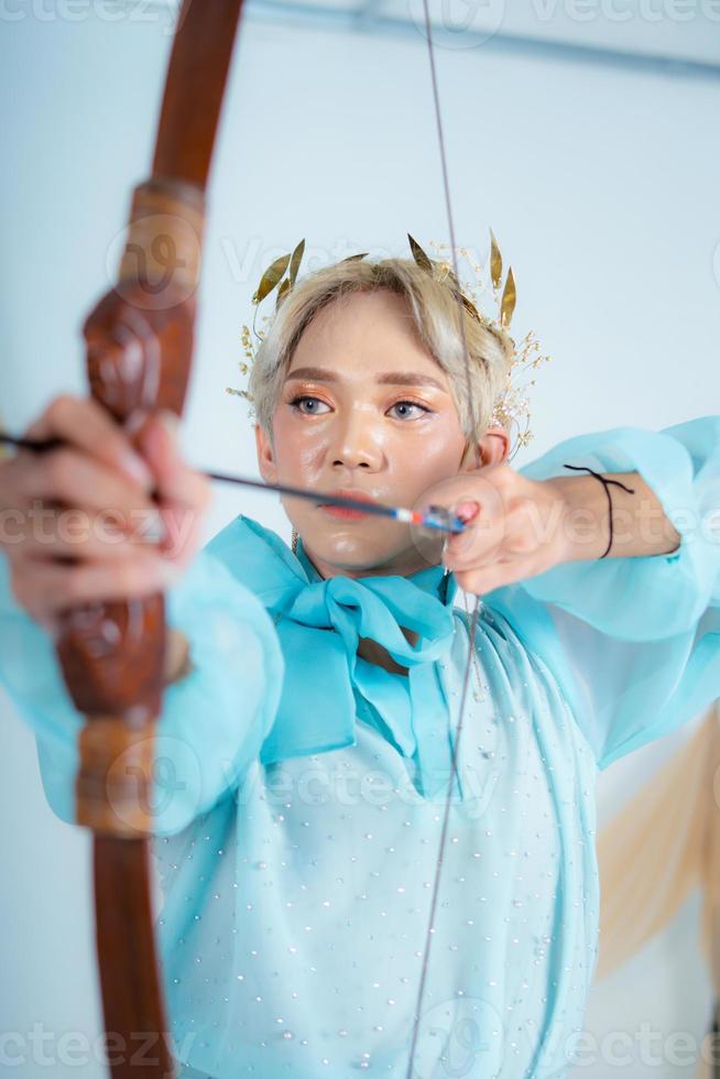 ein asiatisch Frau mit blond Haar halten ein Pfeil während tragen ein Blau Kleid foto