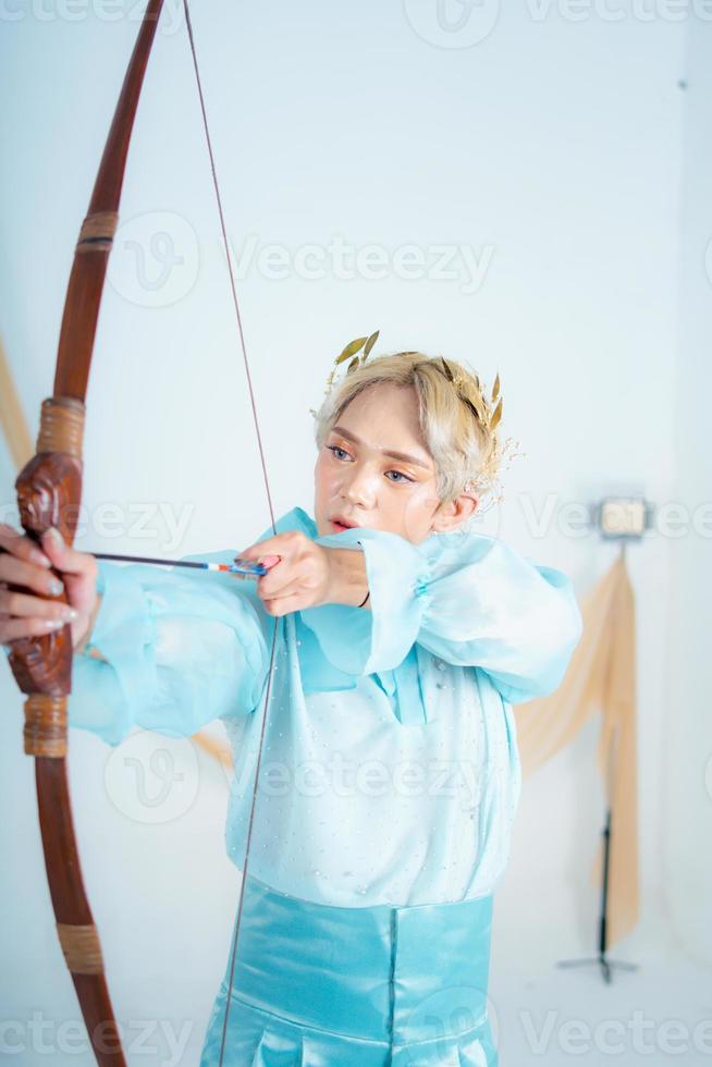 ein Prinzessin im ein Blau Kleid ziehen ein Bogen mit ihr Hand foto