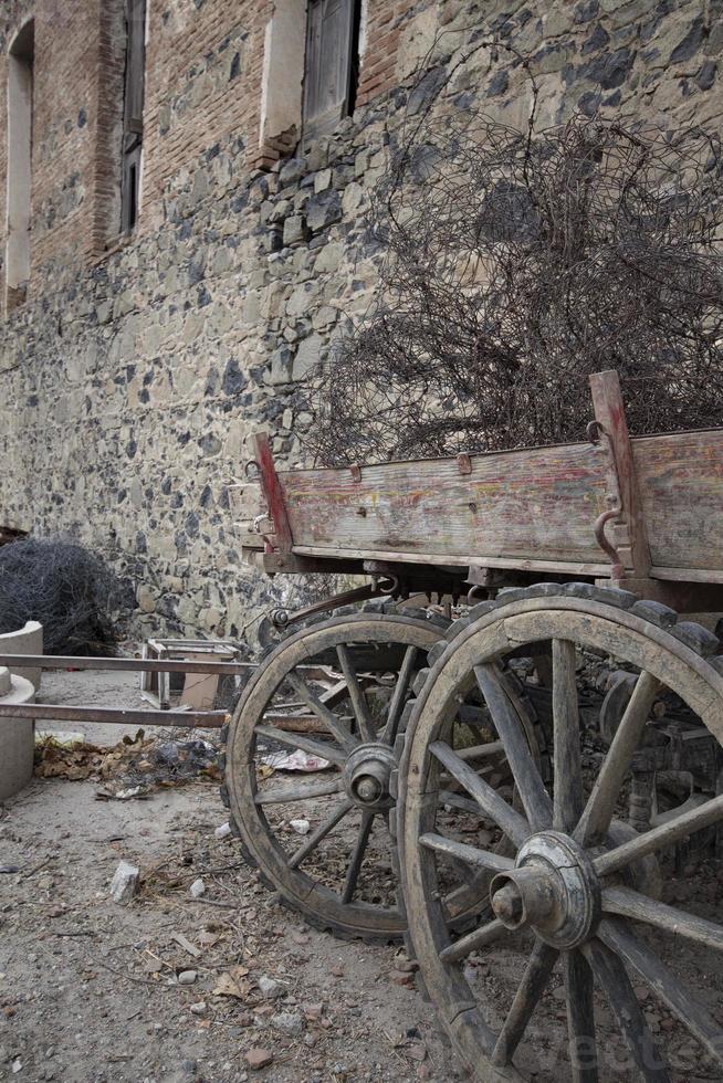 alt hölzern Wagen im Vorderseite von ein alt Stein Mauer im das Dorf. geparkt hölzern Wagen, traditionell ländlich Transport, historisch Objekte, Antiquität hölzern Wagen Räder. foto