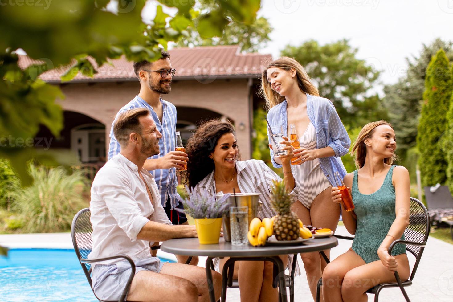 Gruppe junger Leute, die mit Apfelwein am Pool im Garten jubeln foto