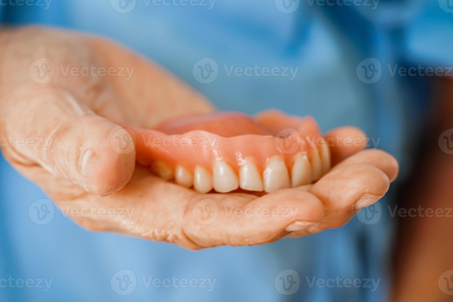 asiatisch Senior Frau geduldig halten Zähne Prothese im ihr Hand zum kauen Lebensmittel. foto