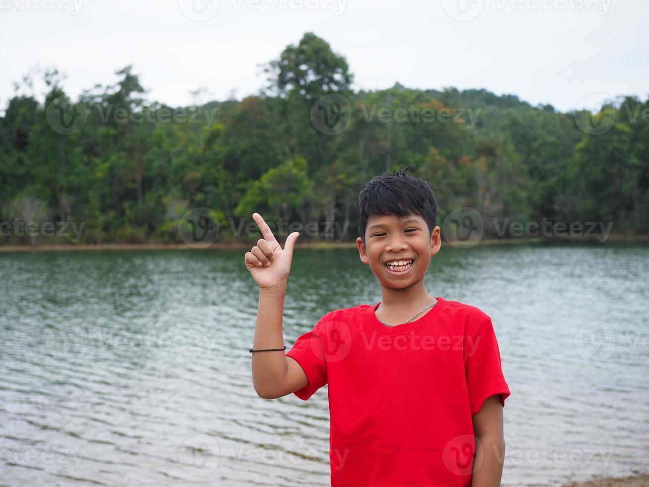 Der Junge lächelte und deutete mit der Hand auf seine Seite. im Hintergrund ist ein Reservoir. foto