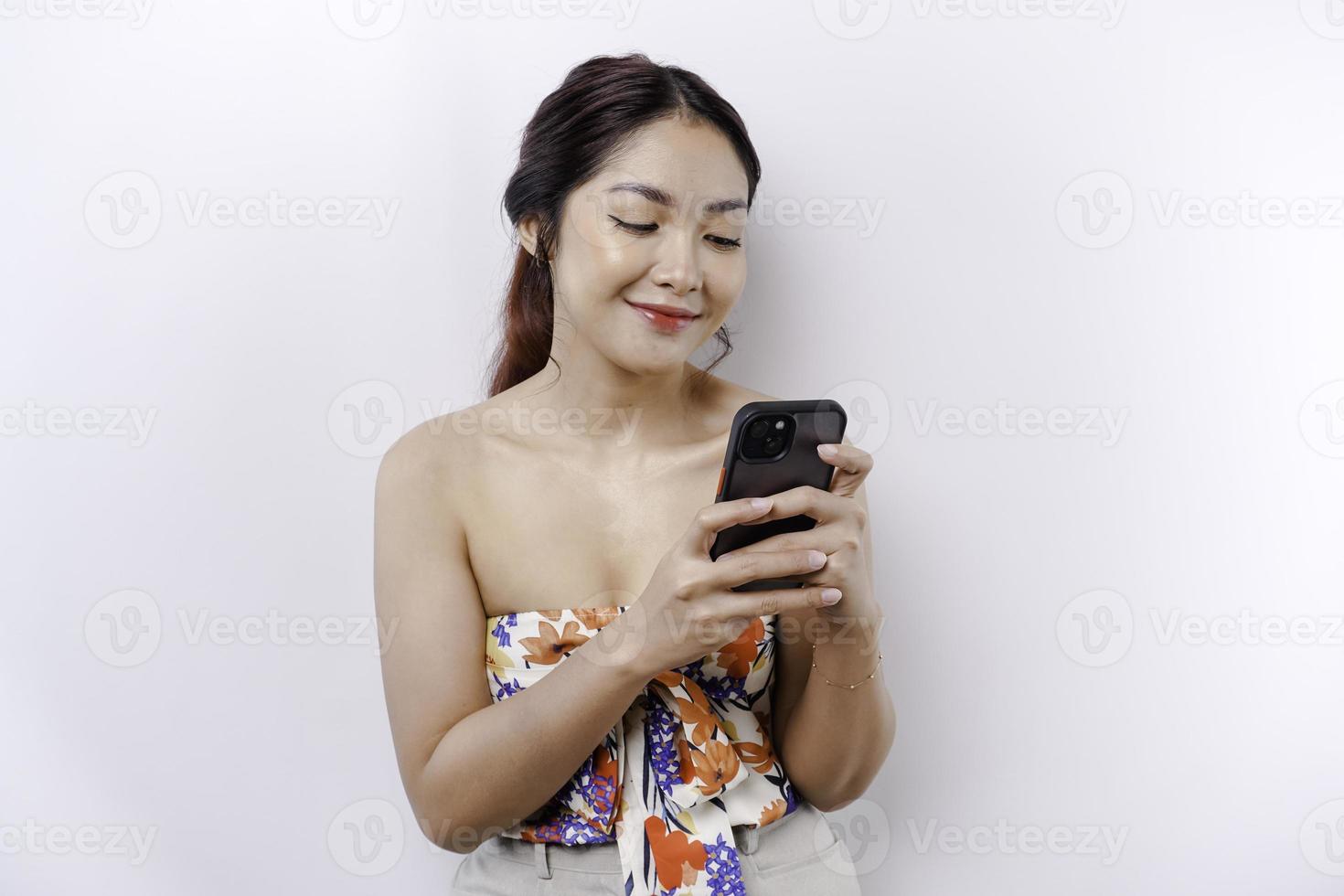 ein Porträt von ein glücklich asiatisch Frau halten ihr Telefon, isoliert durch Weiß Hintergrund foto